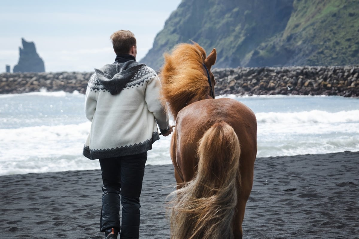 Man and horse walking on the black beach, next to Icewear store in Vík