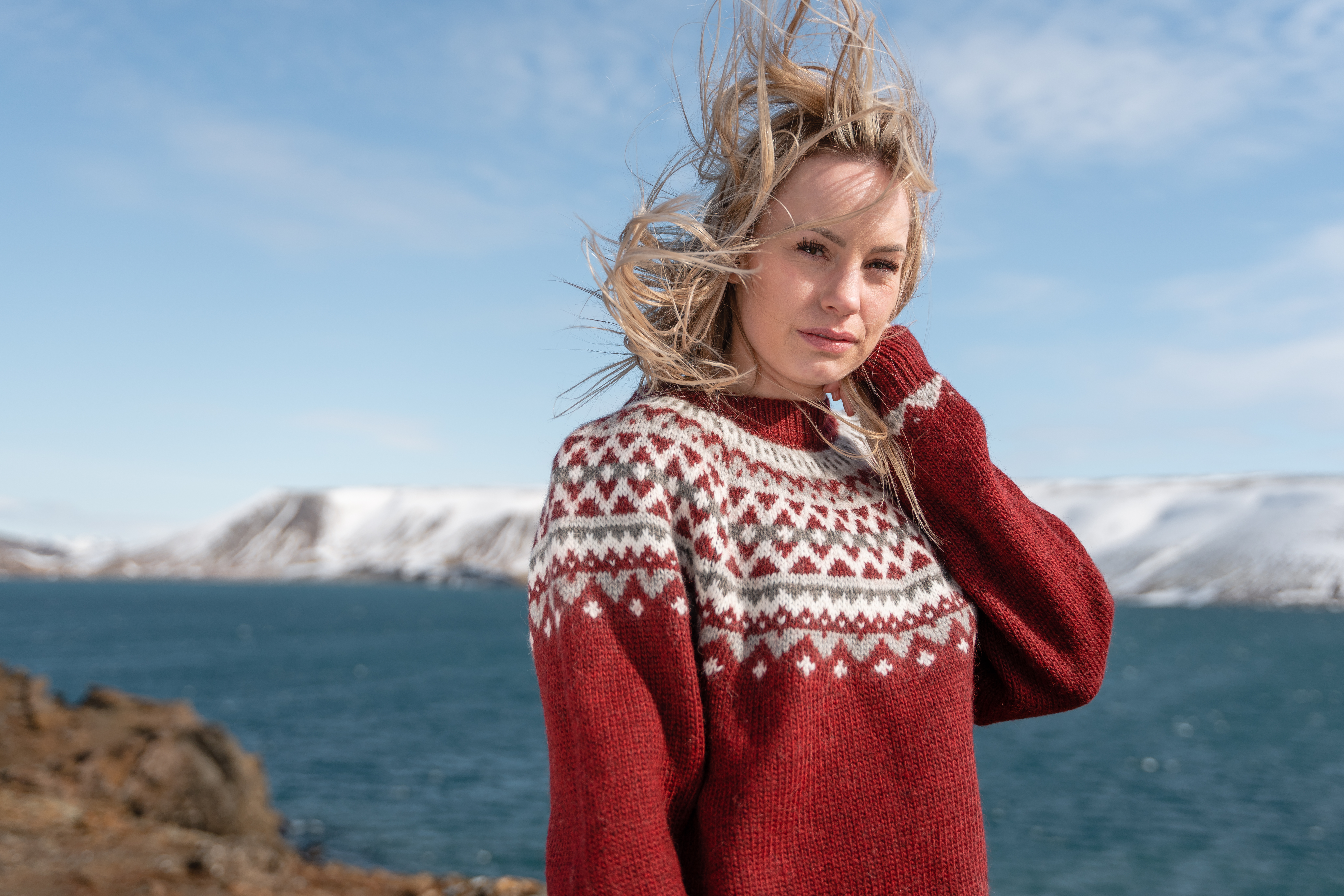 woman in Icelandic sweater, sea and mountain behind her