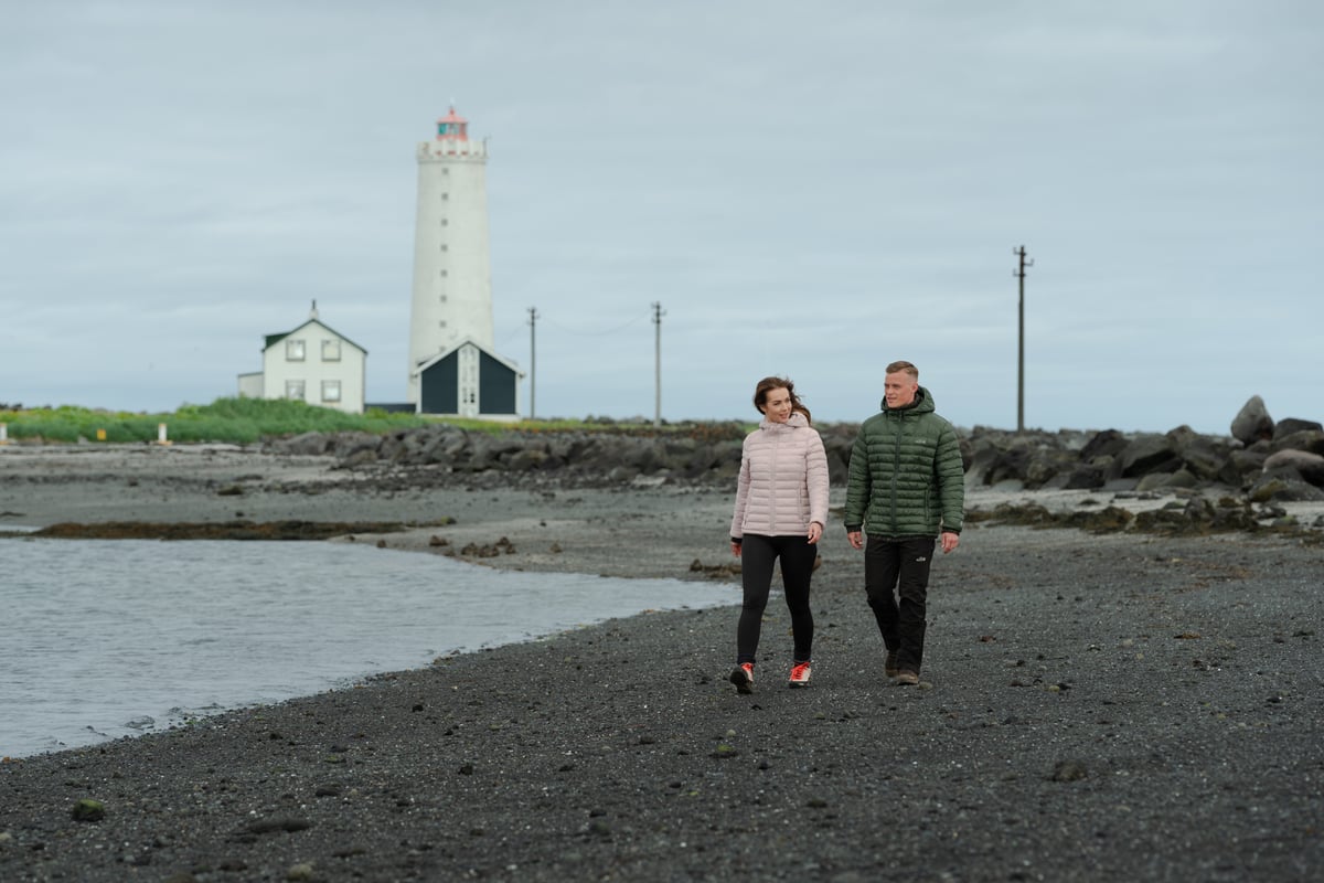 Un couple se promenant sur la plage, un vieux phare derrière eux