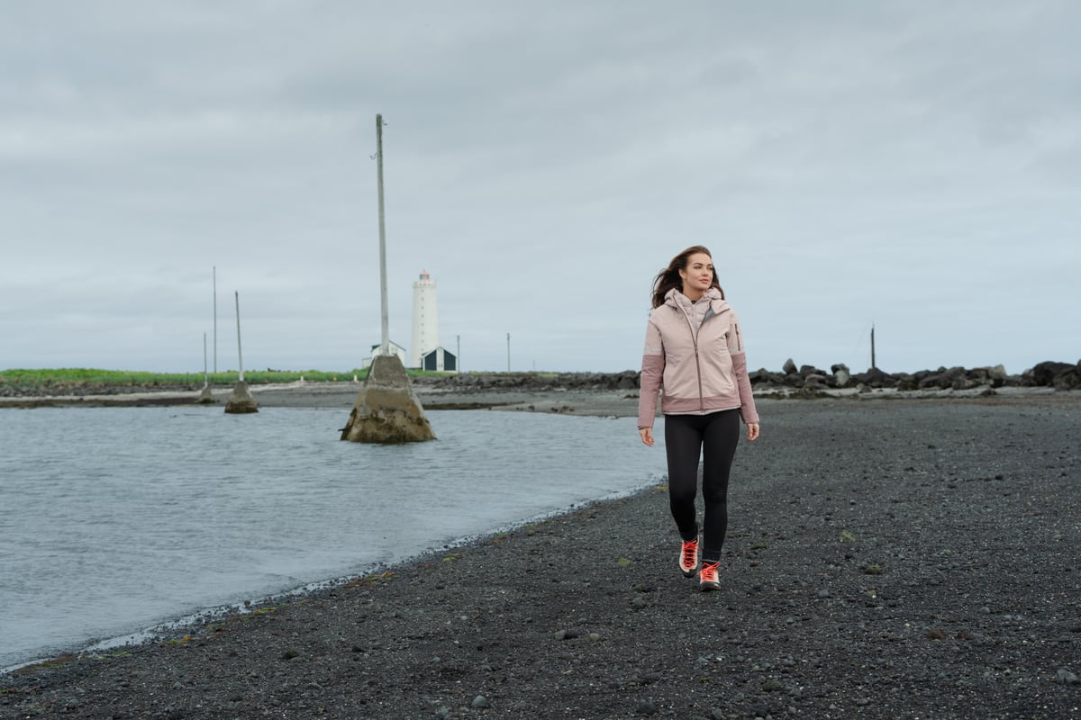 woman walking on the beach, old light house behind her