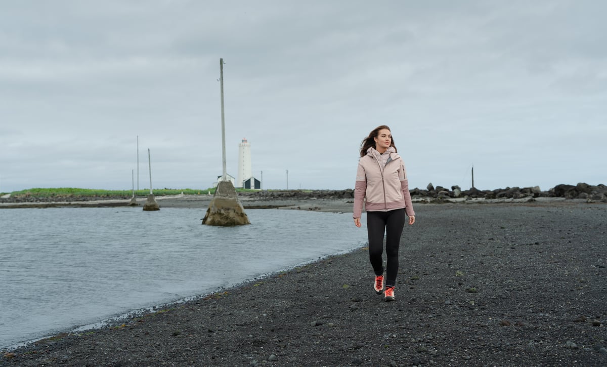 woman walking on the beach, old light house behind her
