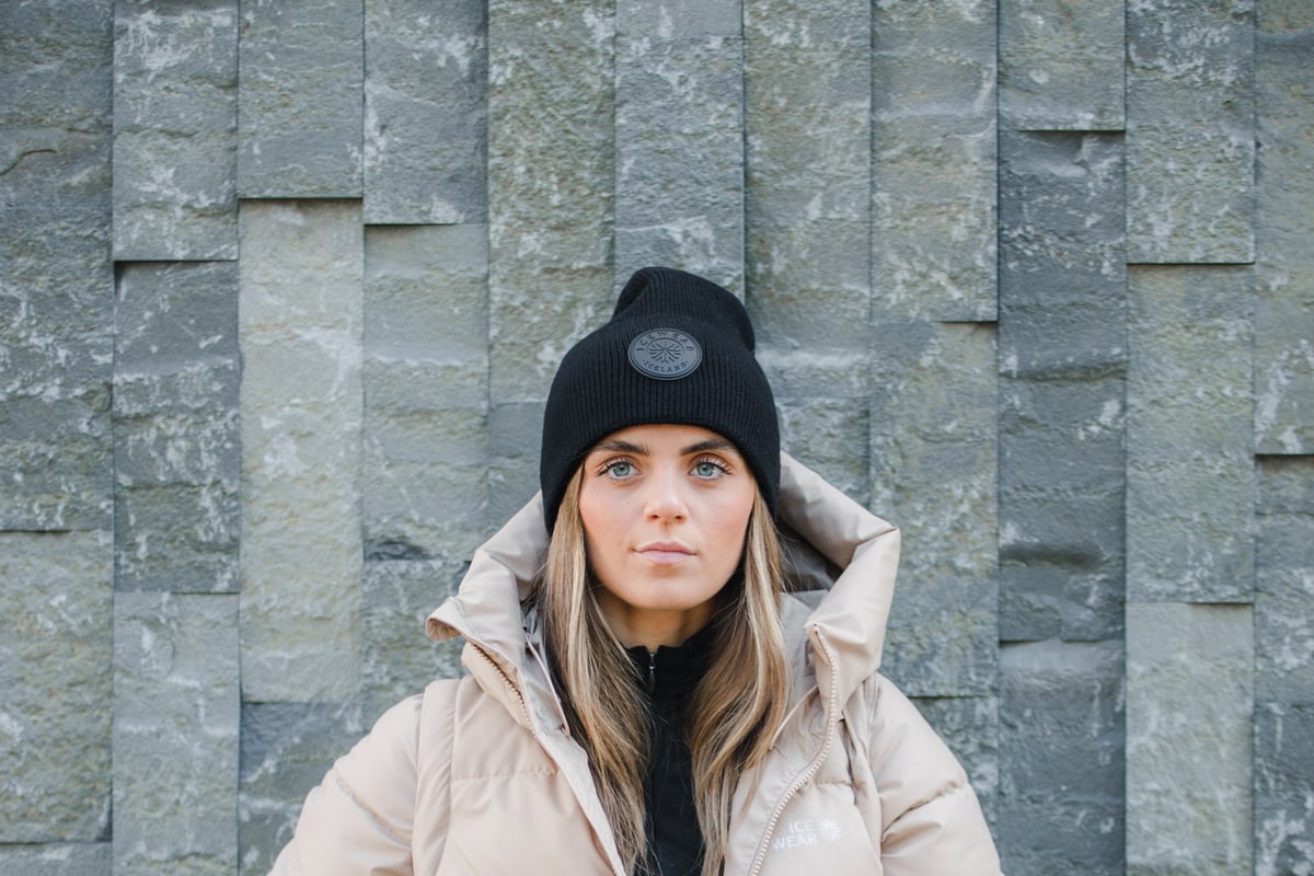 Une femme en manteau chaud debout contre un mur de pierre