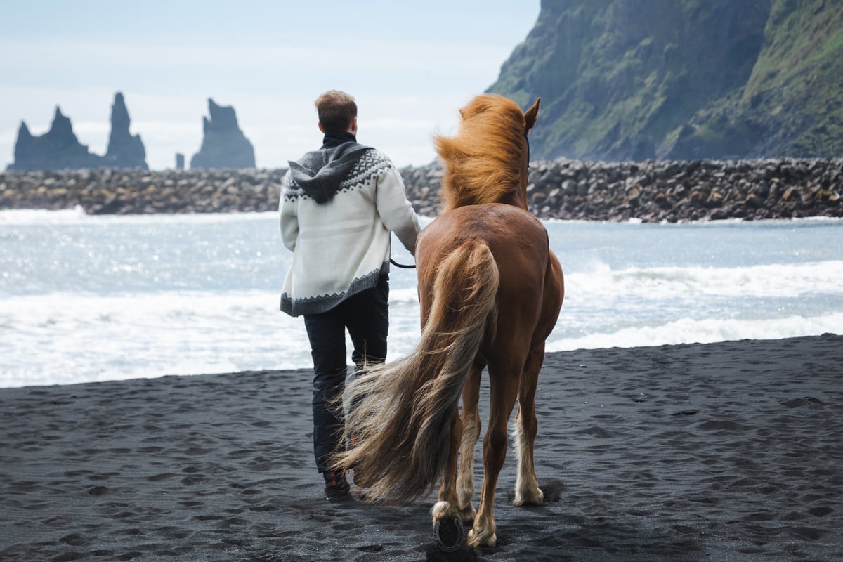 man and horse walking on black beach