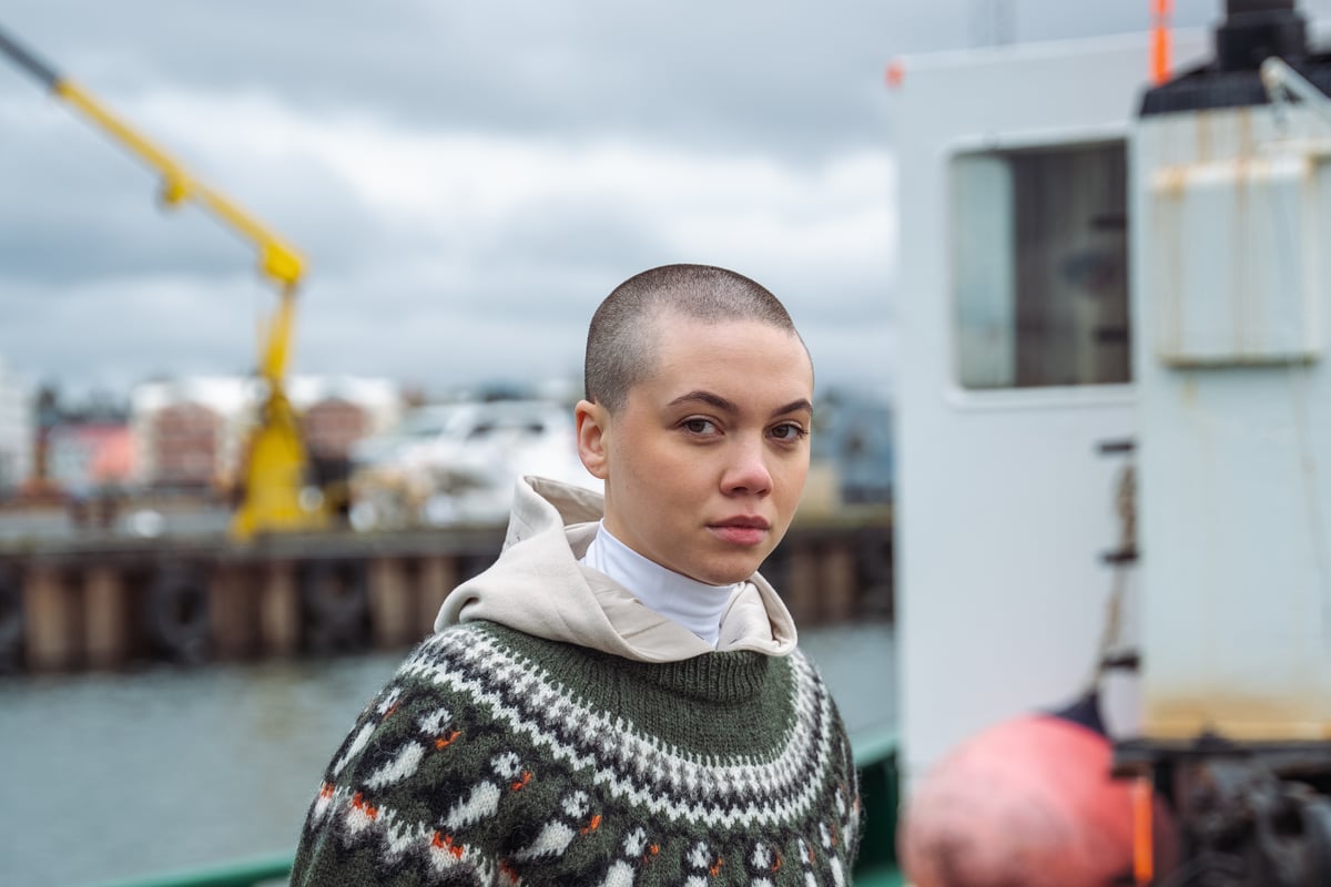 Eine Frau an einem Boot, die einen Wollpullover mit Papageientauchermuster trägt