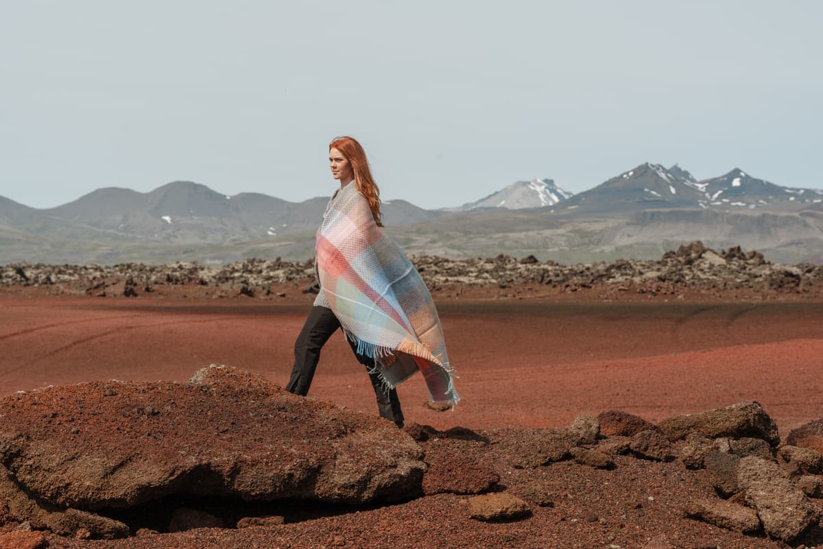 Une femme avec une couverture autour d’elle sur du sable rouge, ouest de l’Islande