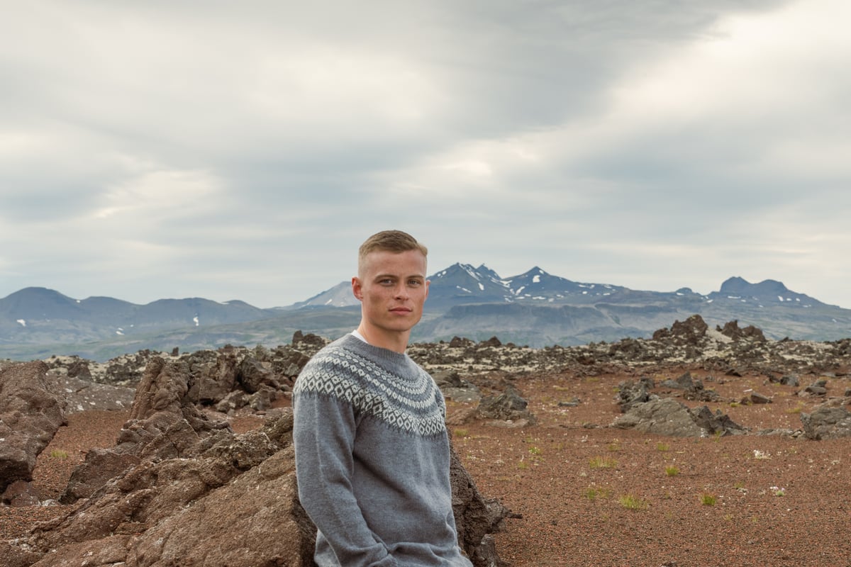 Un homme se tient près d’un rocher, une grande zone montagneuse derrière lui