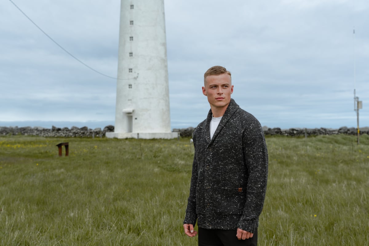 man in a gras field and light house behind him